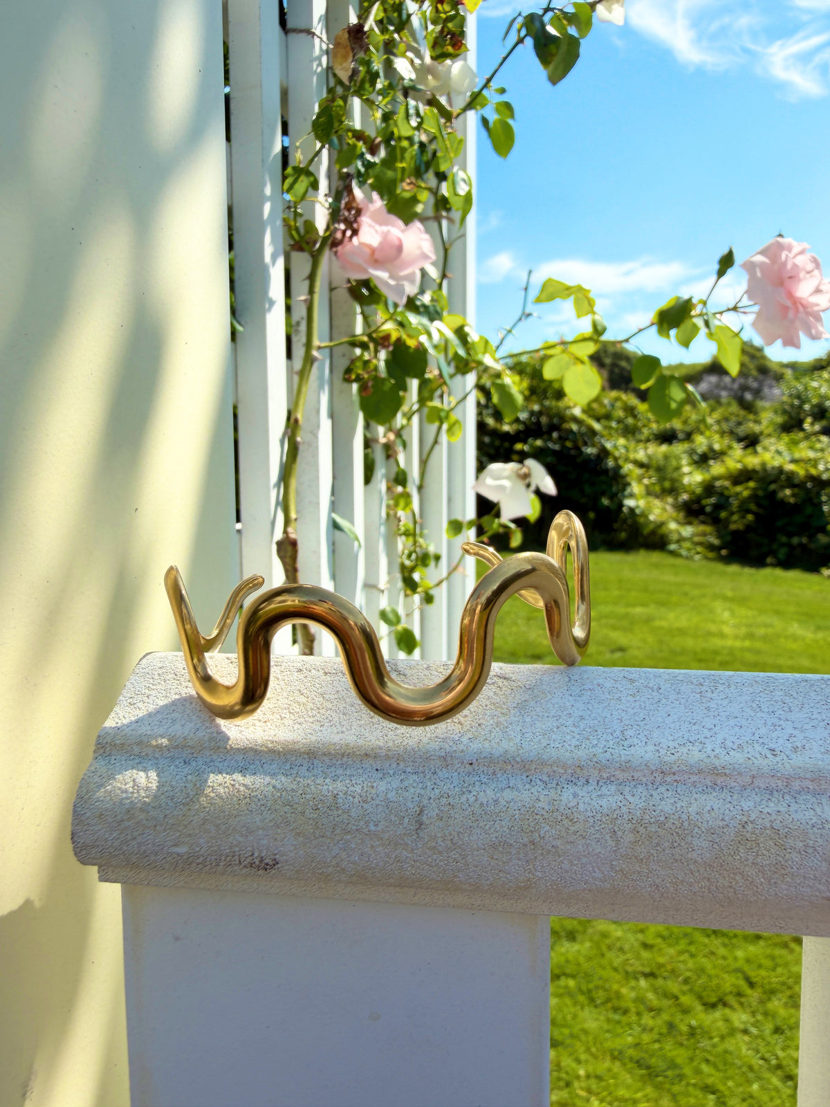 Wavy gold cuff resting on a sunlit porch railing