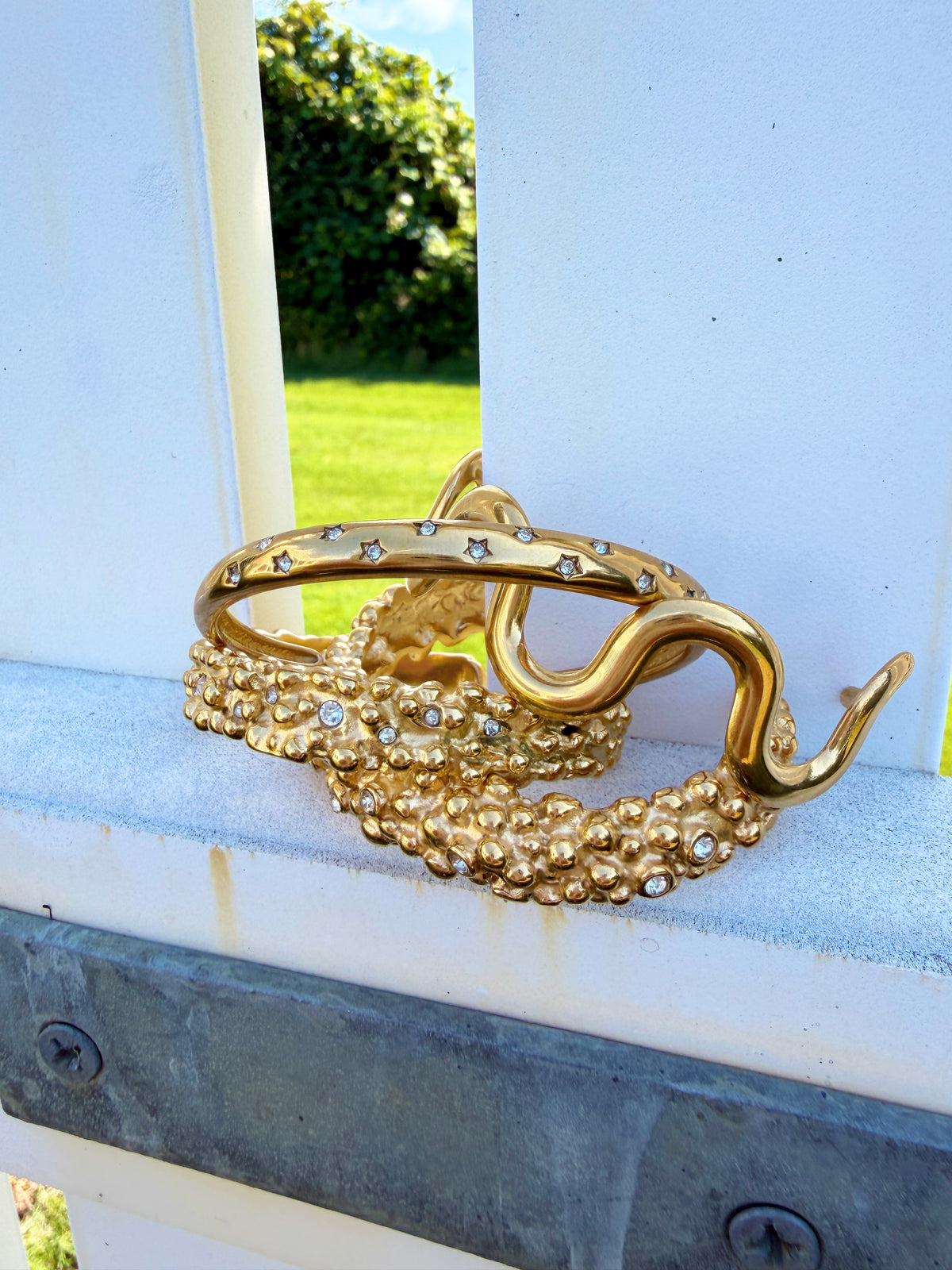 Wavy and textured gold cuffs on a blue porch railing