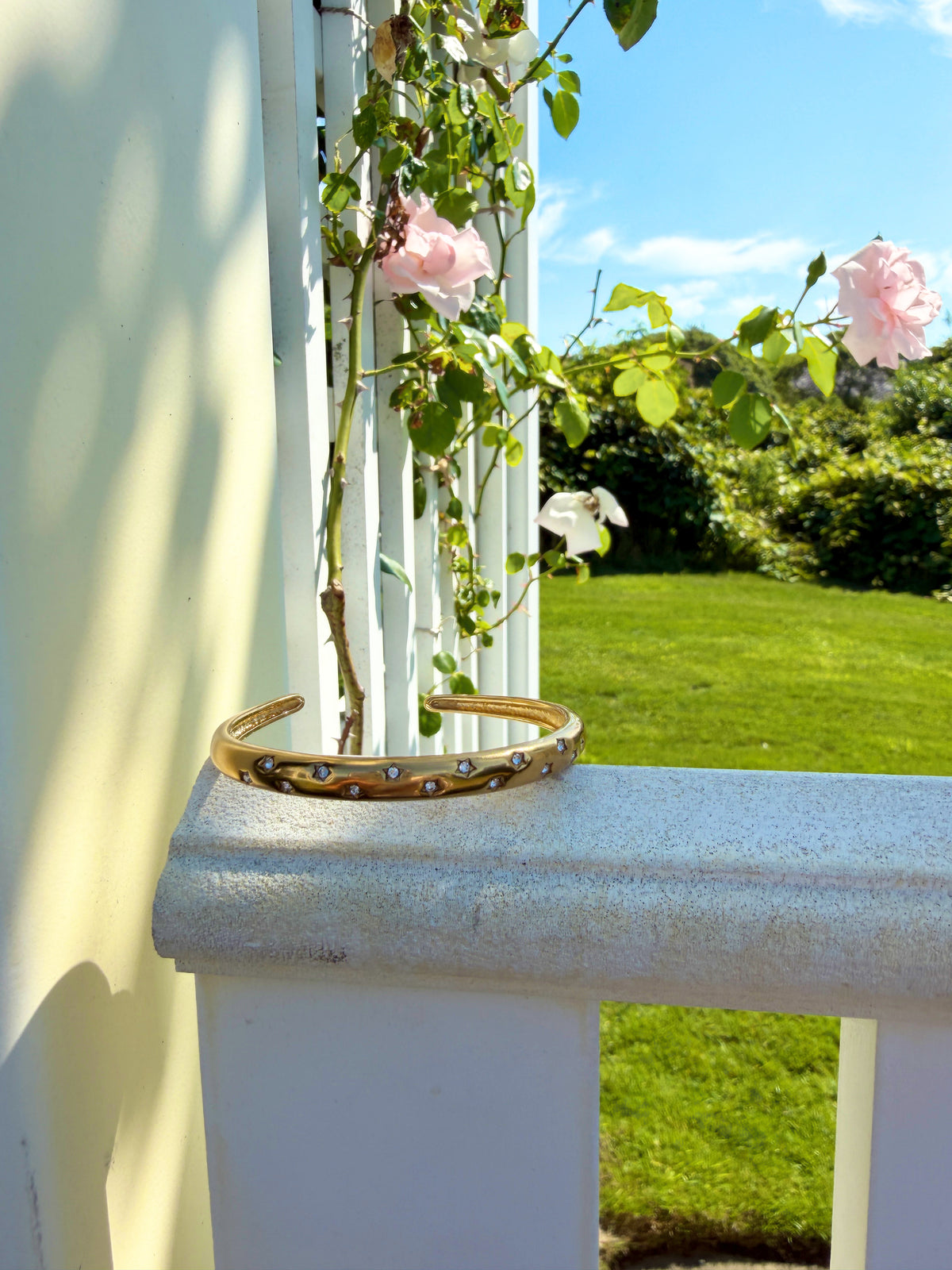 Gold cuff bracelet resting on a sunlit porch railing