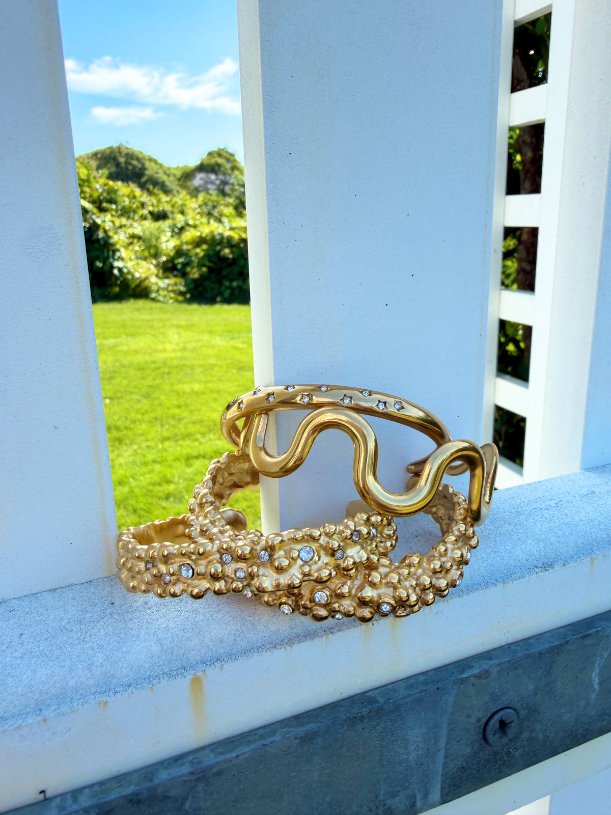 Wavy and textured gold cuffs on a blue porch railing