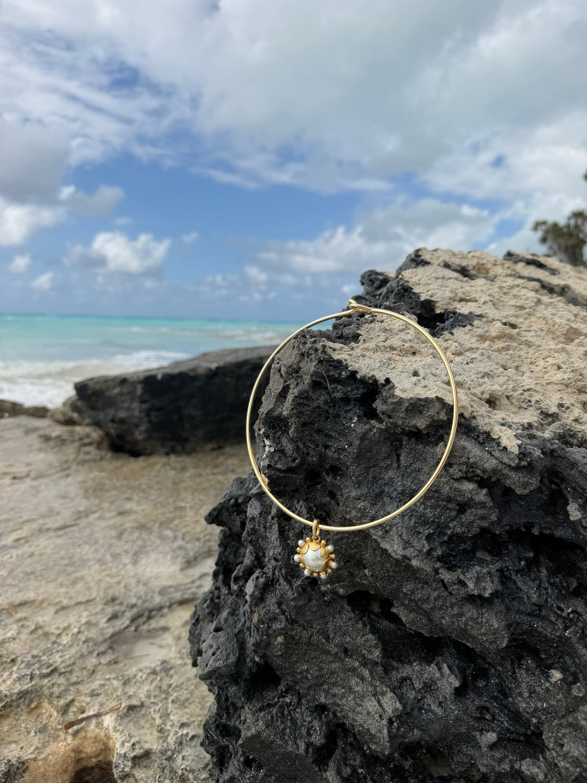 Gold Mida collar draped on rocks beside the ocean