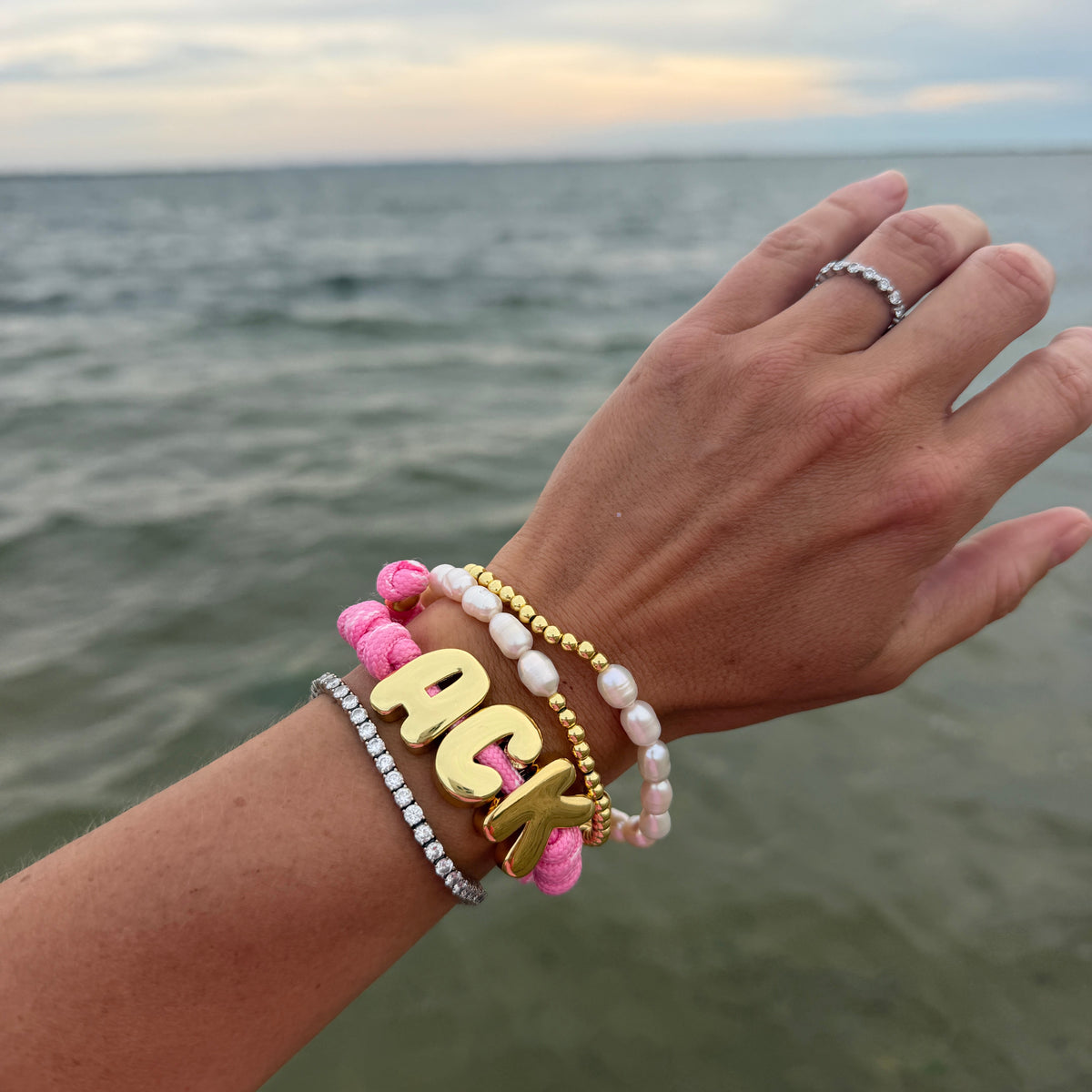 ACK paracord bracelet worn in a layered wrist stack beside the ocean