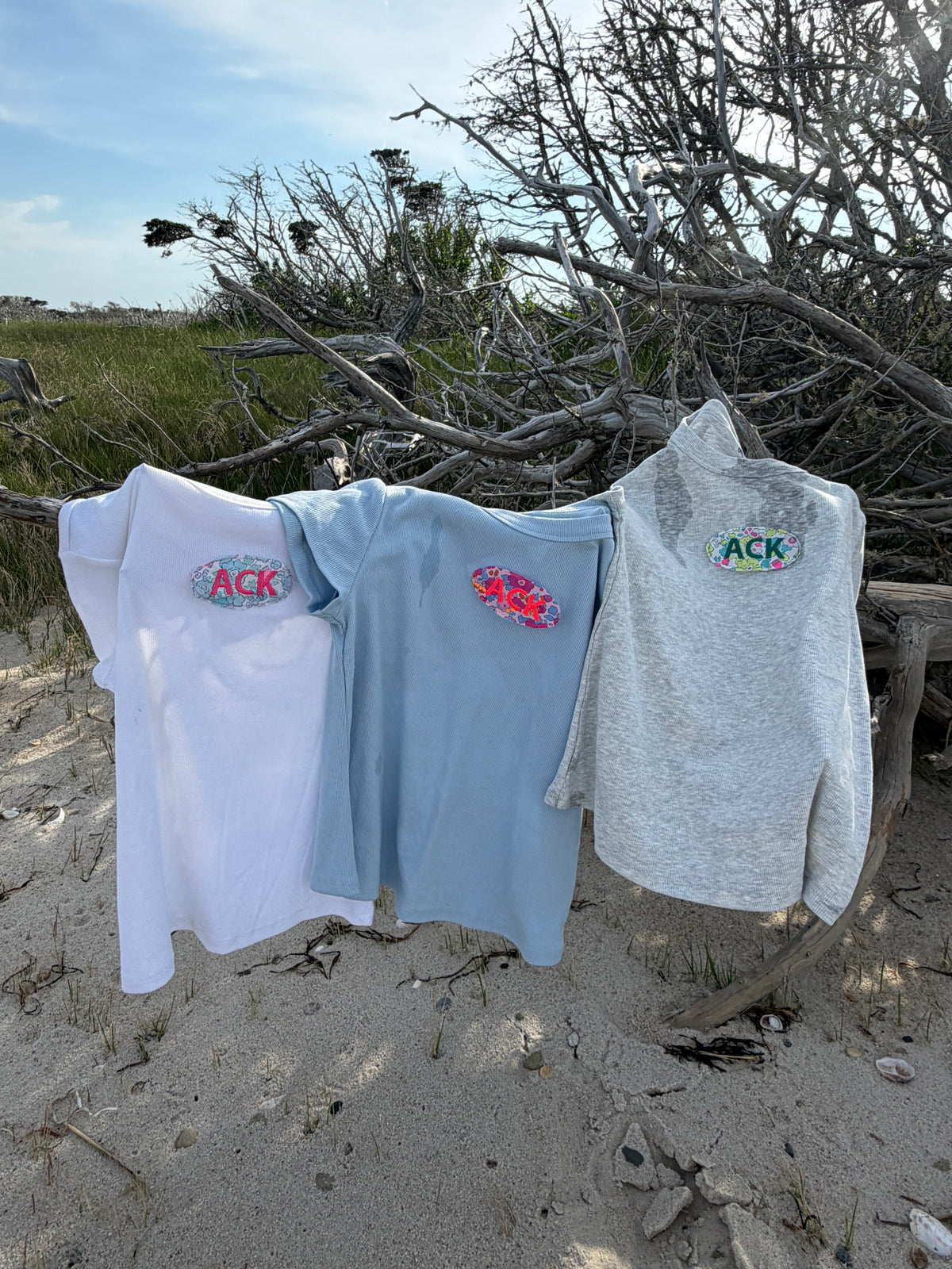 White, blue, and grey personalized tees hanging outdoors