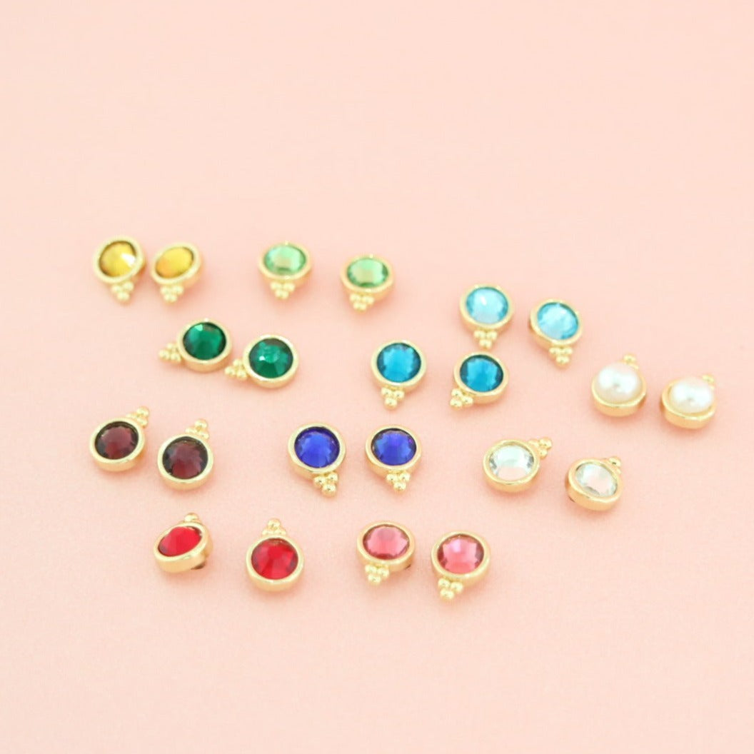 Fortuna stud earrings in assorted colors on a pink background