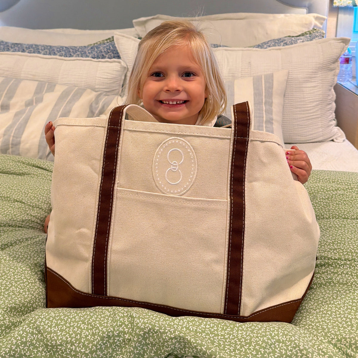 A child sitting inside an oversized canvas tote with brown straps