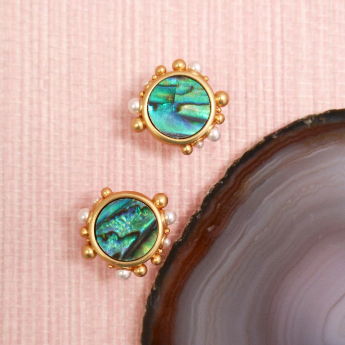 Abalone Porto stud earrings in gold settings on a pink background
