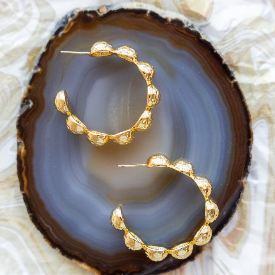 Gold Florence hoop earrings arranged on a dark agate slice