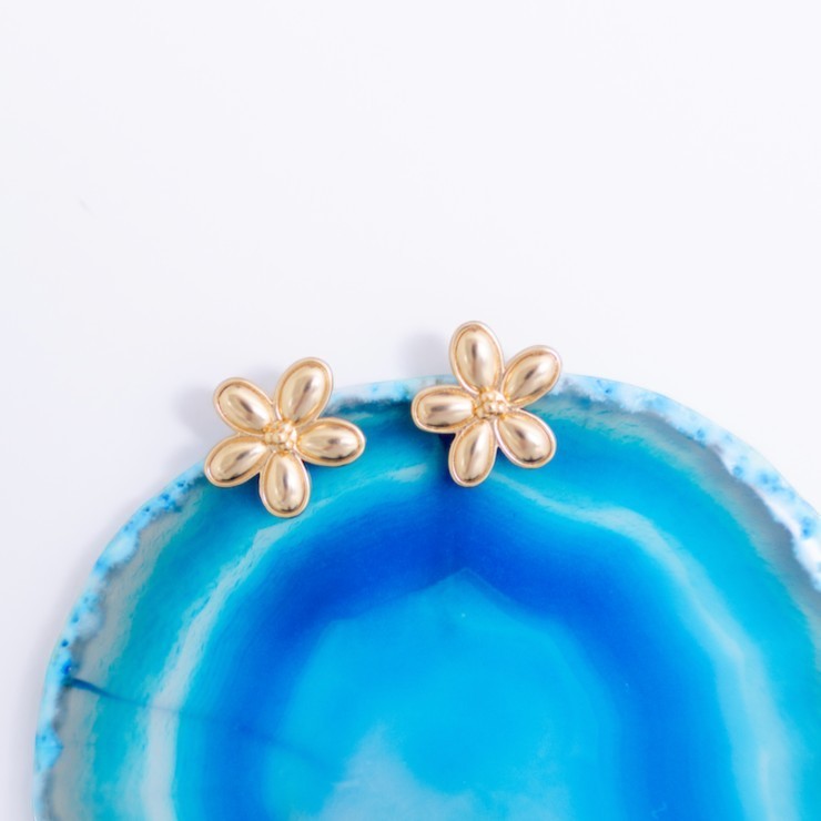 Gold Flora flower stud earrings on a blue agate slice