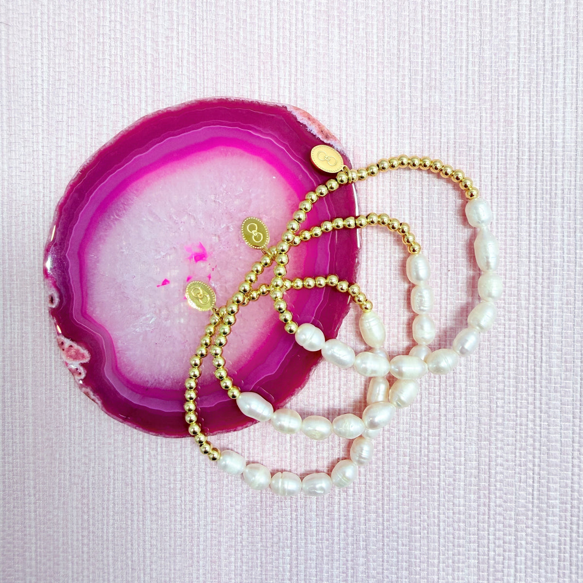 Anna bracelets with gold beads and white pearls on a pink agate slice