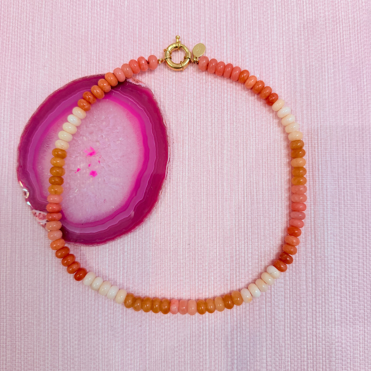 Orange Amalfi beaded necklace arranged on a pink agate slice