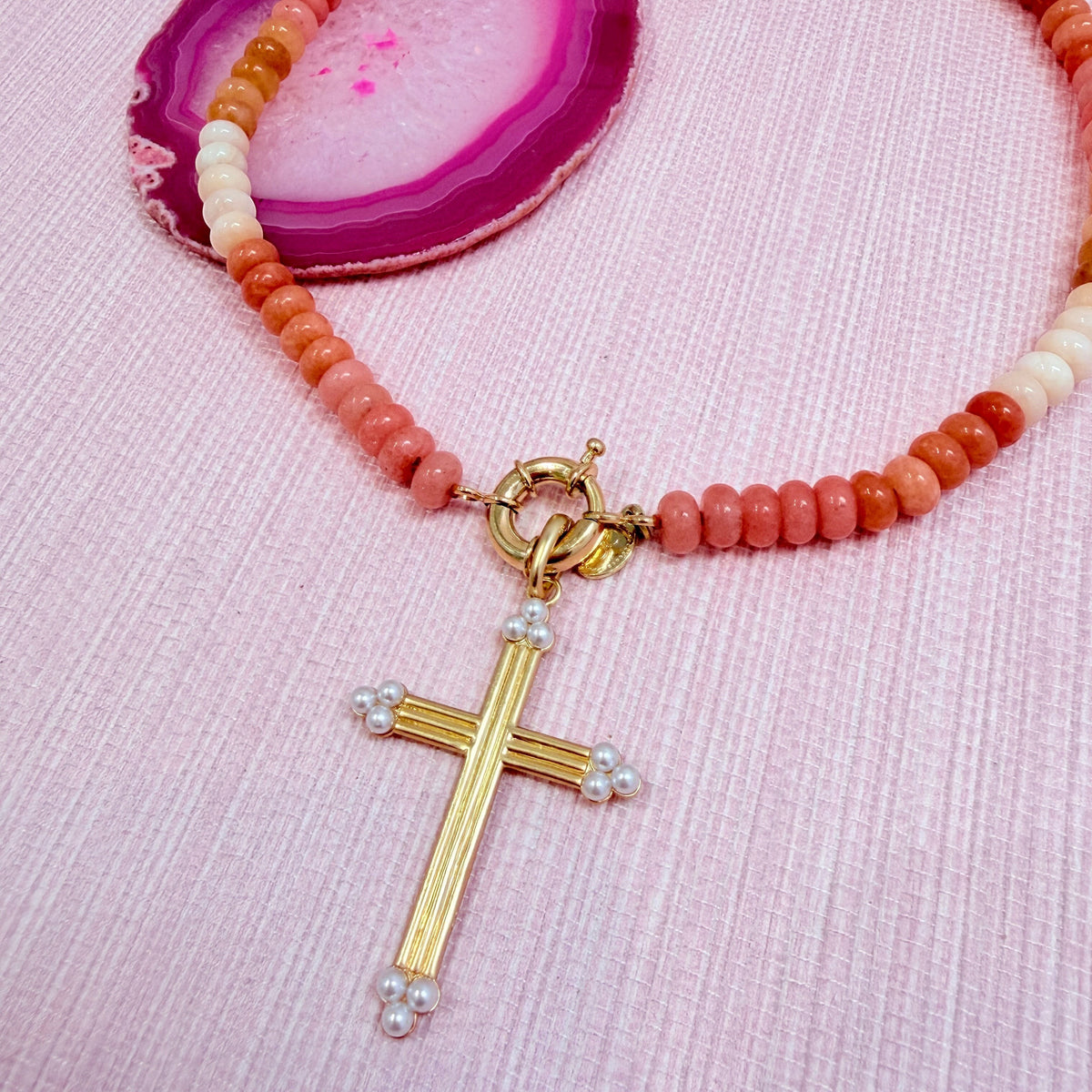 Close-up of a gold cross pendant added to an orange Amalfi necklace