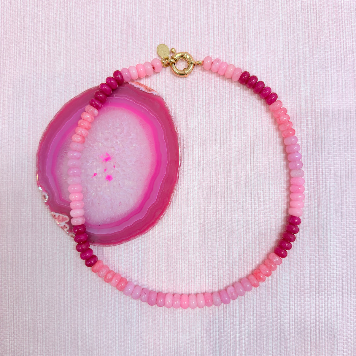 Pink Amalfi beaded necklace arranged around a pink agate slice
