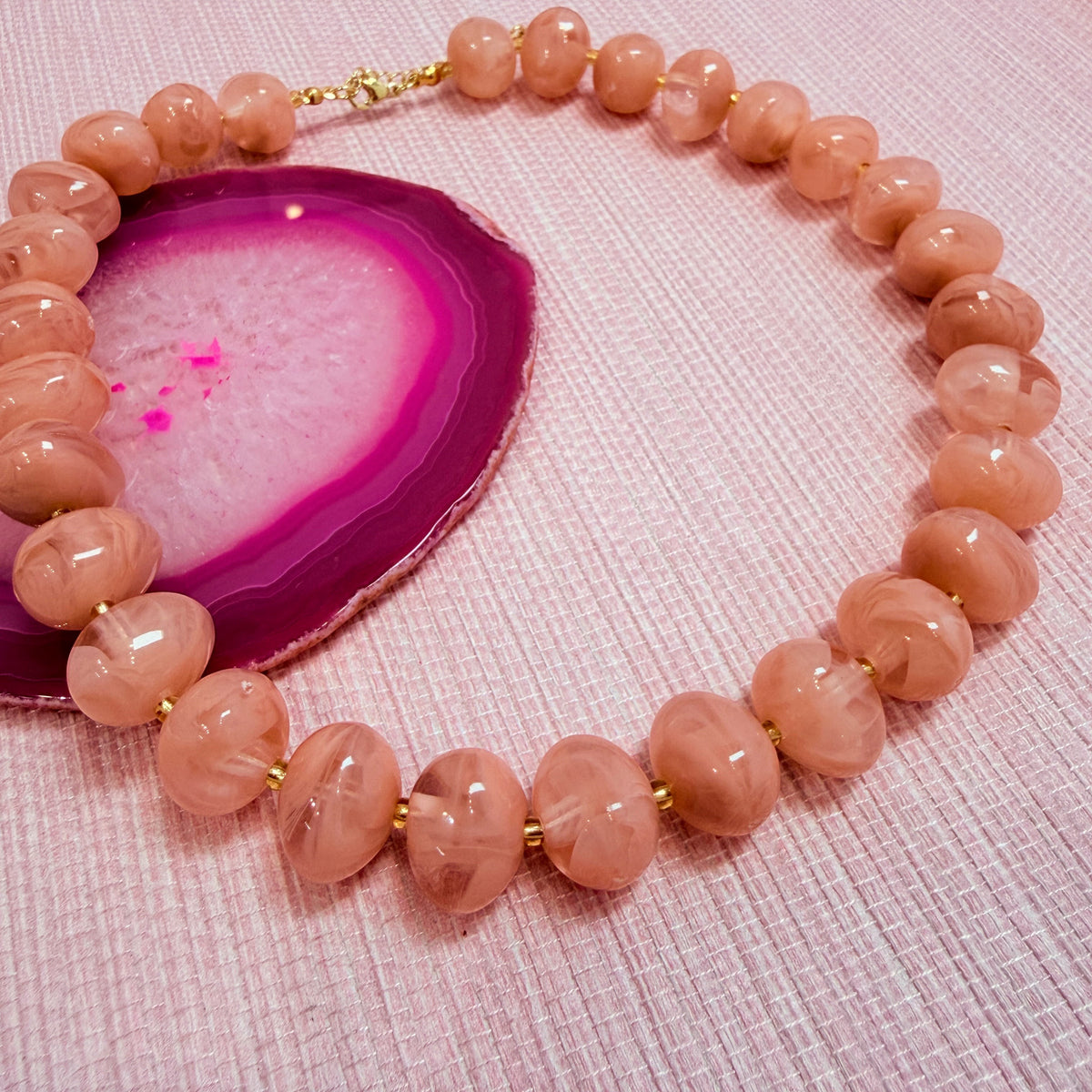 Pink Nardo resin bead necklace arranged on a pink agate slice