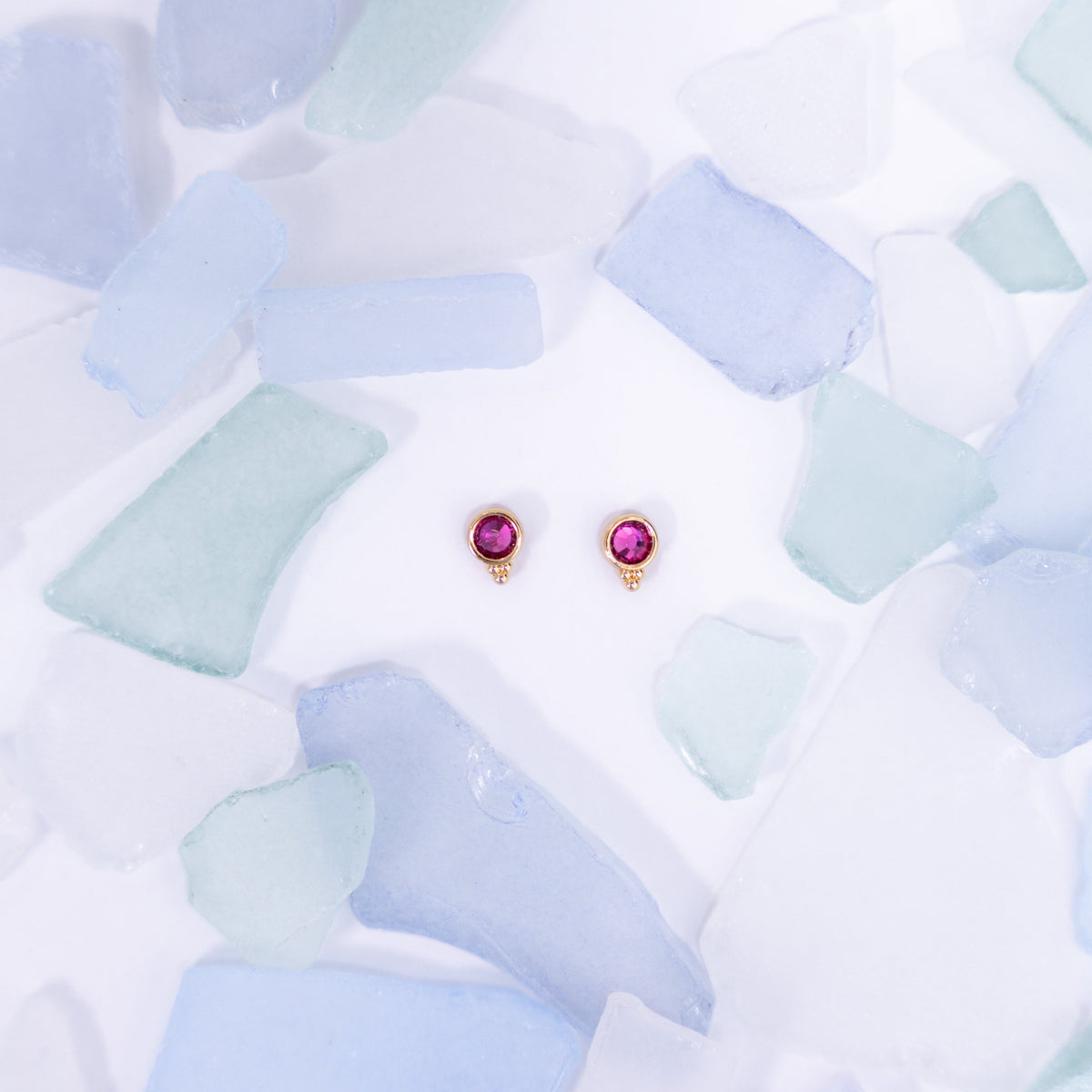 Pair of pink Fortuna stud earrings on a pale blue background