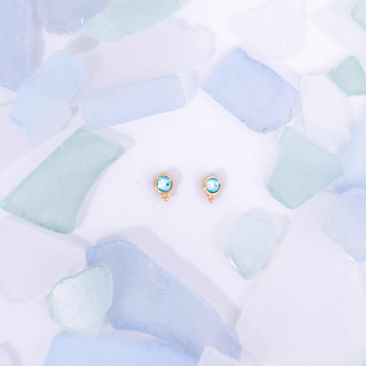 Pair of pale blue Fortuna stud earrings on a pale blue background