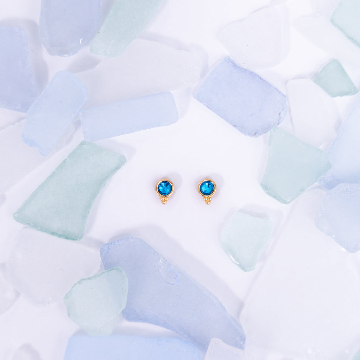Pair of blue Fortuna stud earrings on a pale blue background