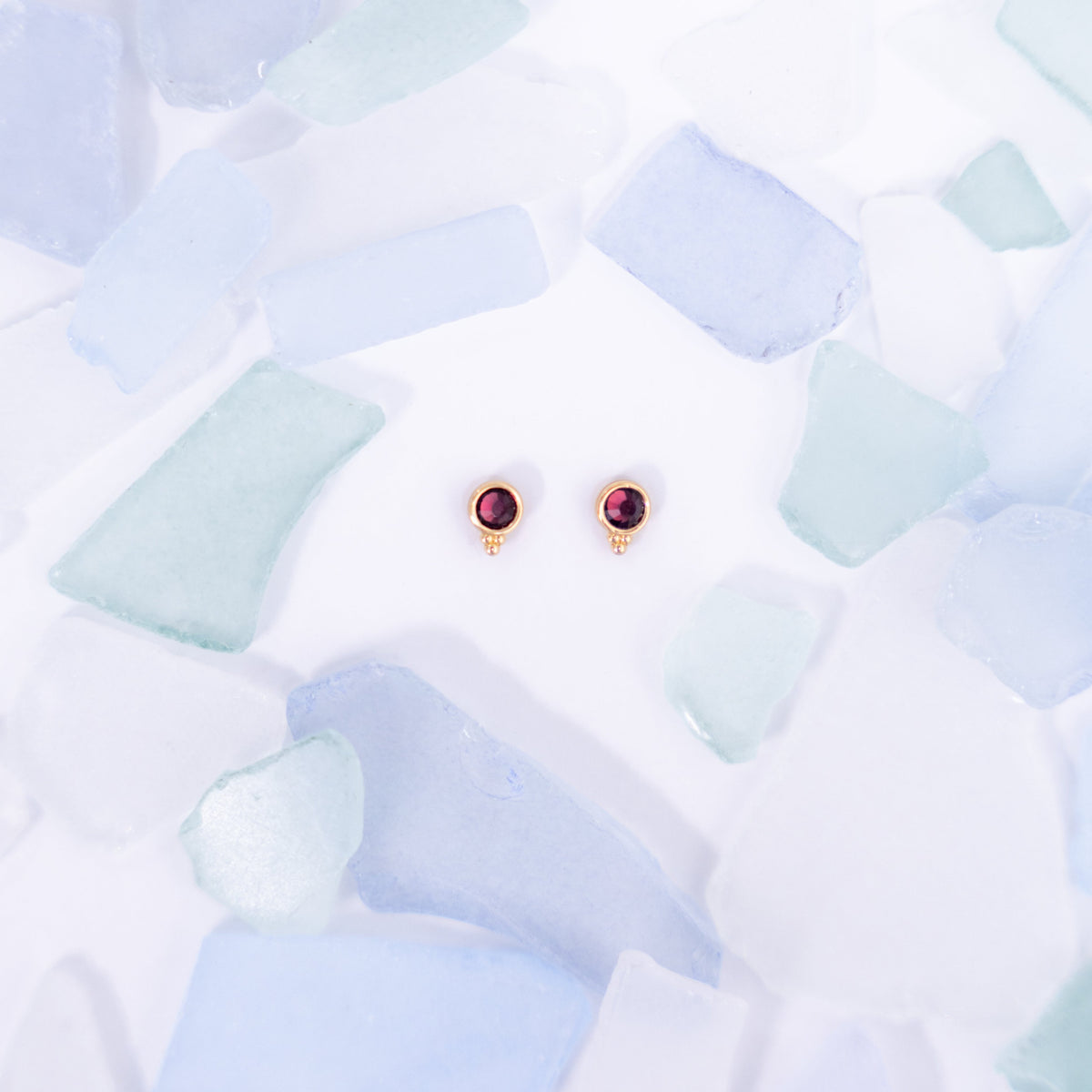 Pair of deep red Fortuna stud earrings on a pale blue background