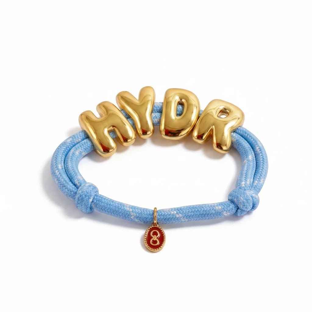 Gresham HYDR adjustable paracord bracelet in powder blue with gold bubble letters and a small red charm.