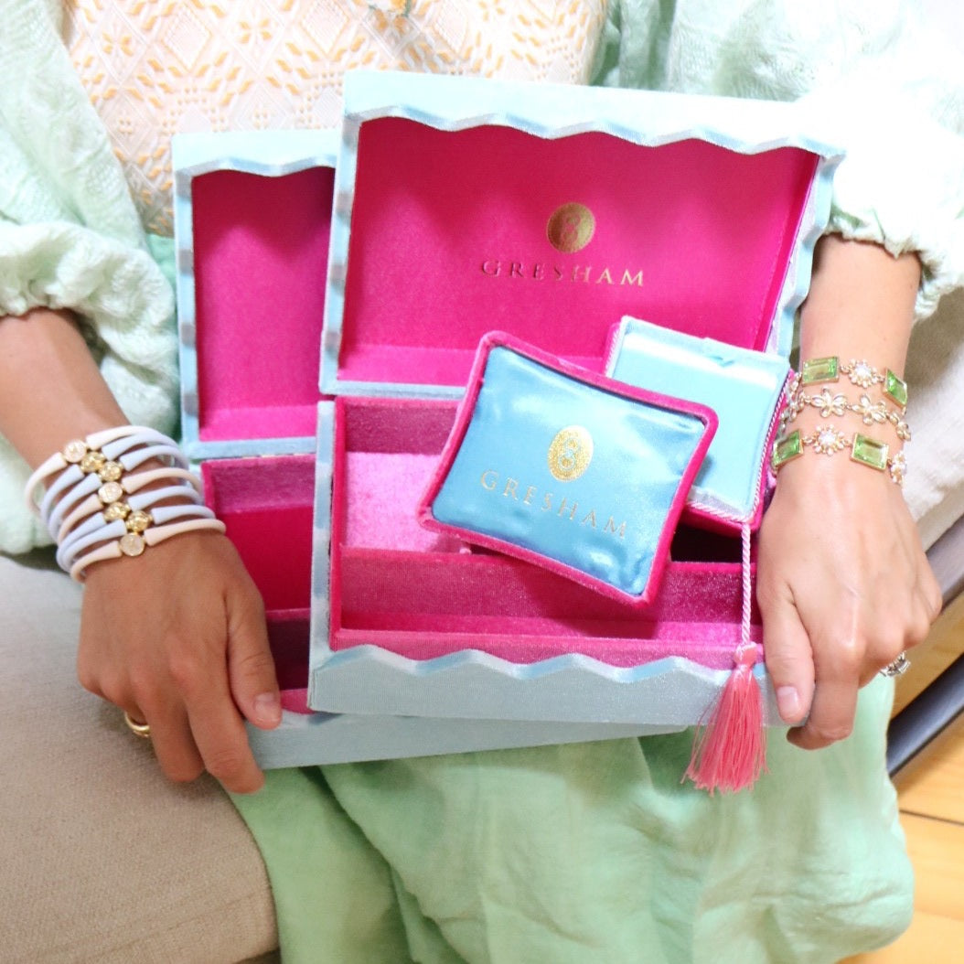 Person holding an open pink jewelry box with a bracelet and jewelry inside