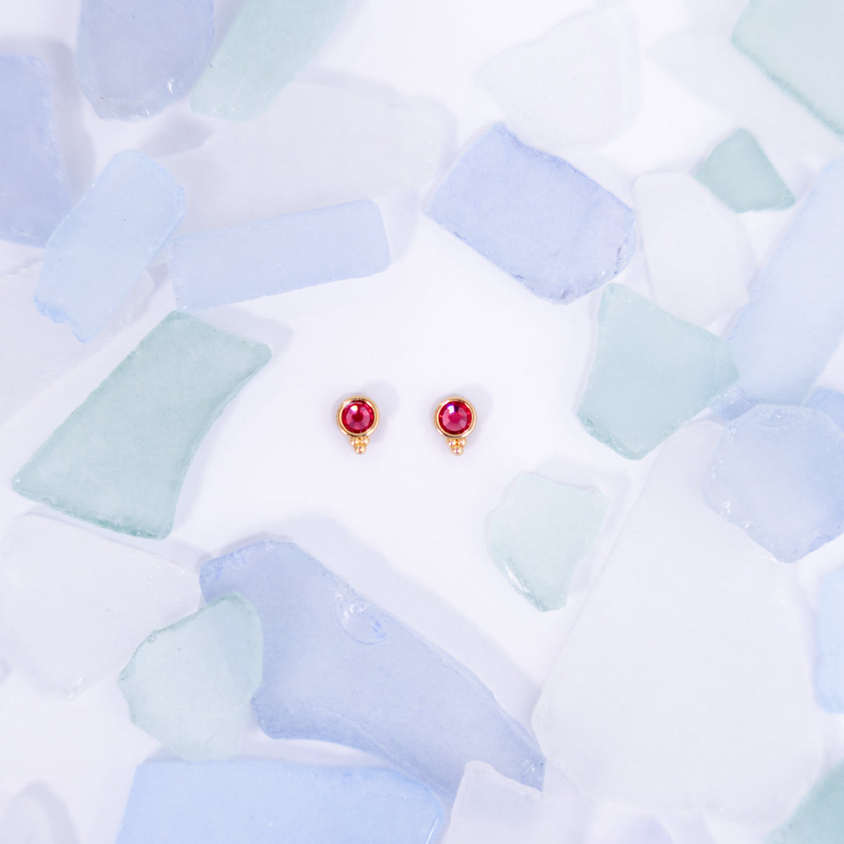 Pair of red Fortuna stud earrings on a pale blue background