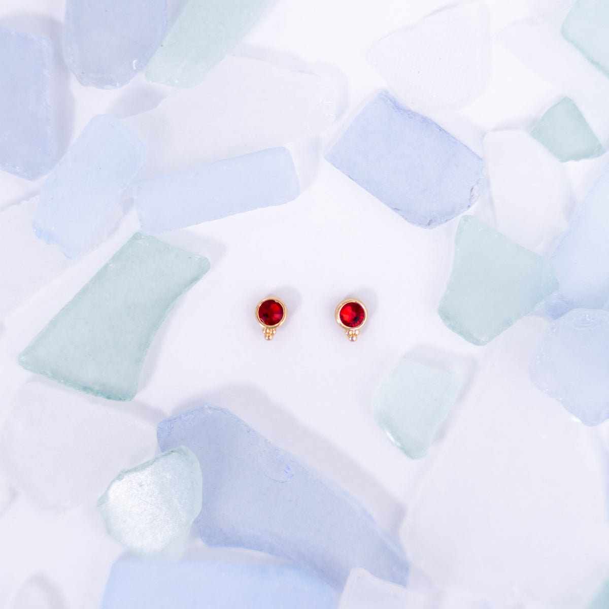 Pair of red Fortuna stud earrings on a pale blue background