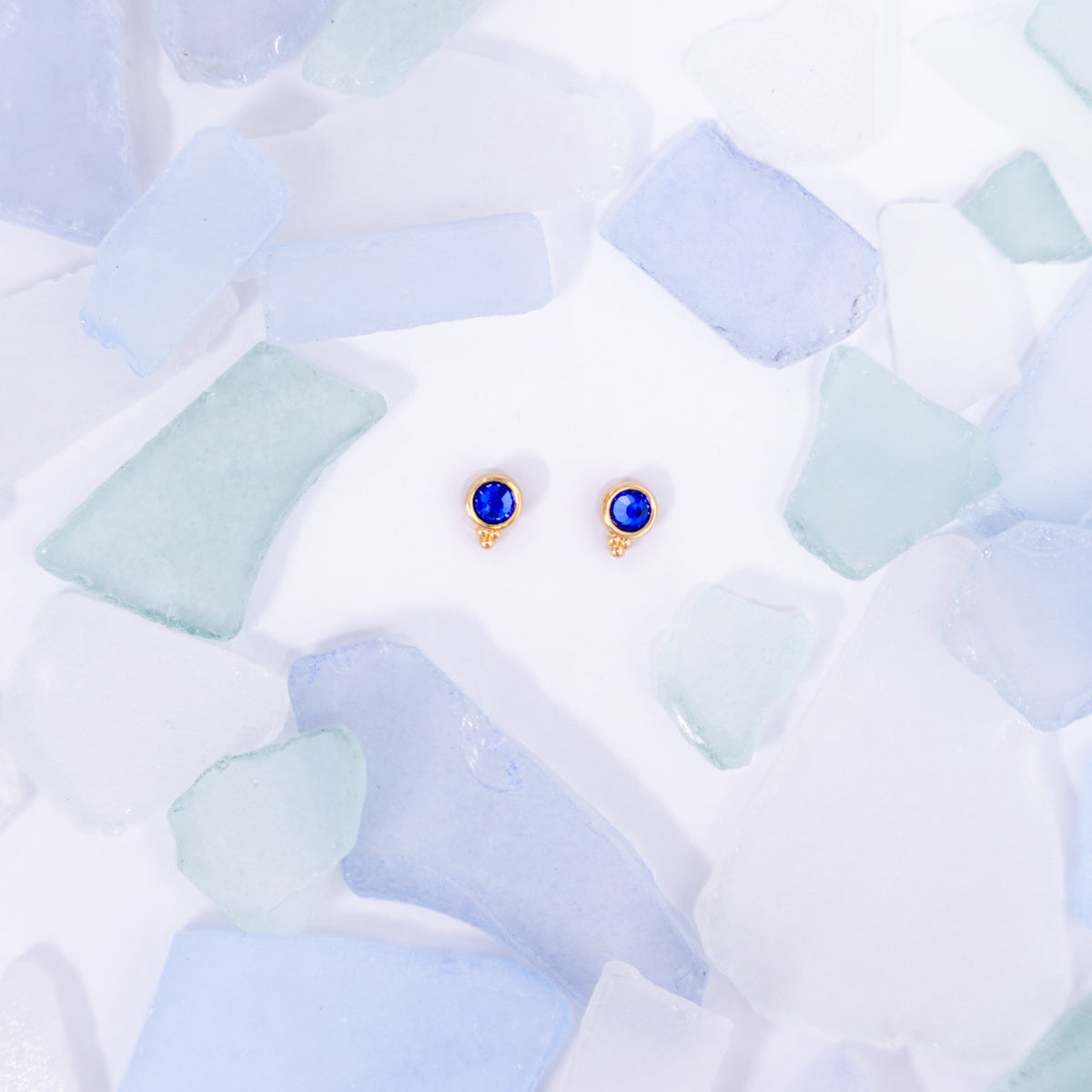 Pair of dark blue Fortuna stud earrings on a pale blue background