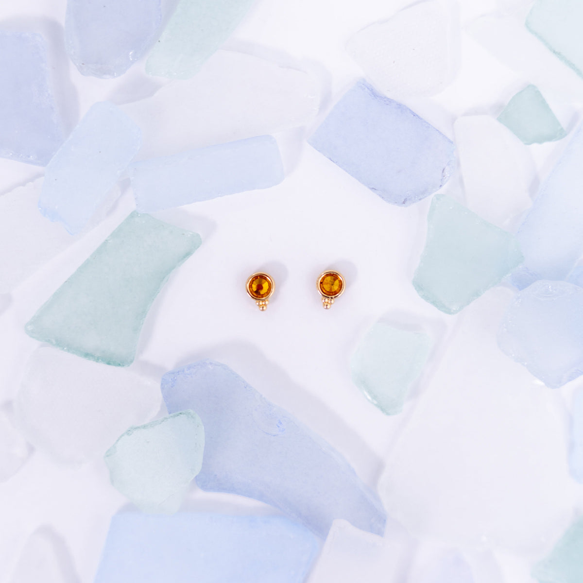 Pair of yellow Fortuna stud earrings on a pale blue background