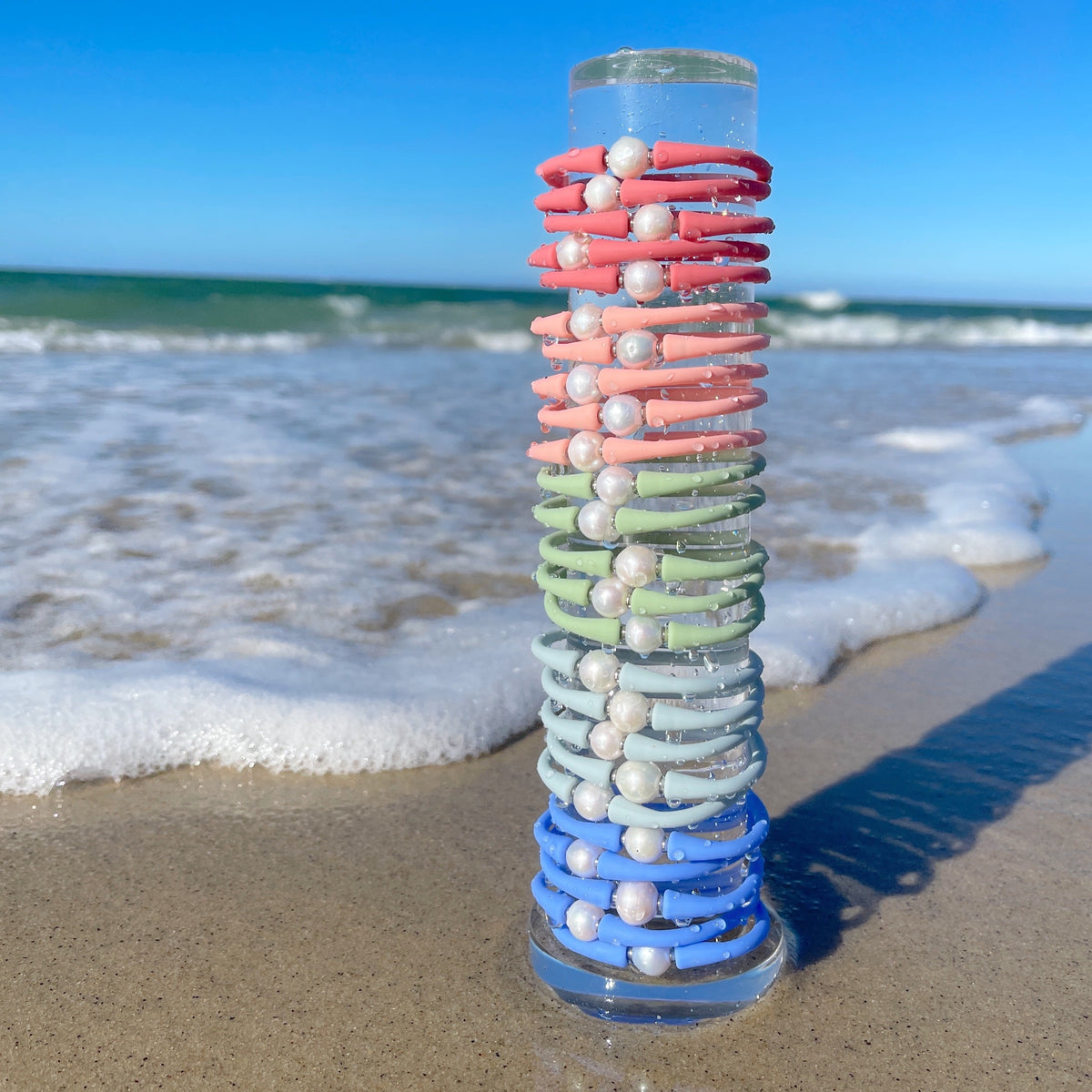 Colorful silicone bracelets stacked on a clear bracelet tower beside the ocean